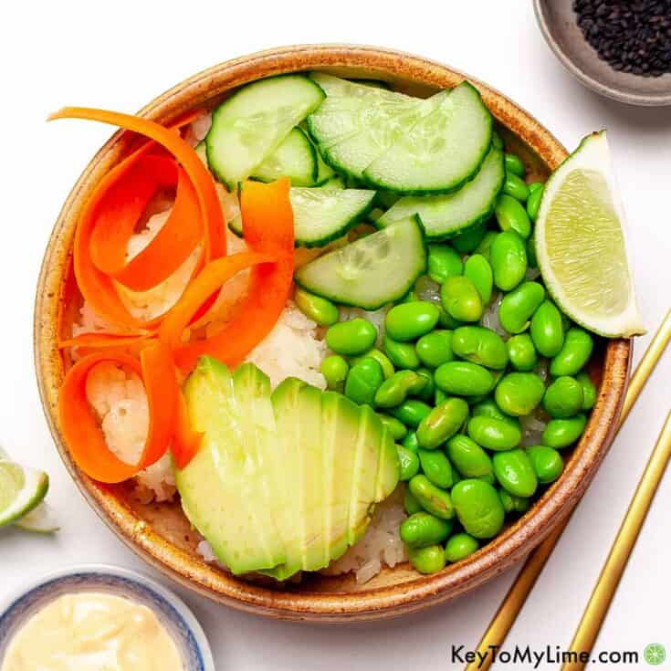 Vegan rice bowl with cucumber, avocado, carrots, edamame, and lime for a healthy plant-based meal.