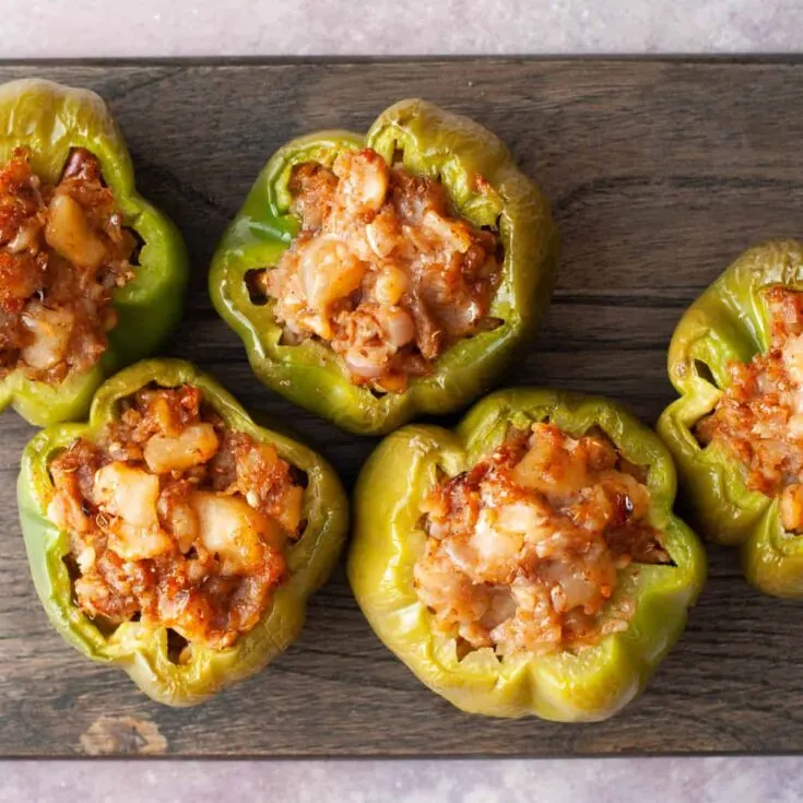 Delicious vegan stuffed green bell peppers with savory filling on wooden surface.