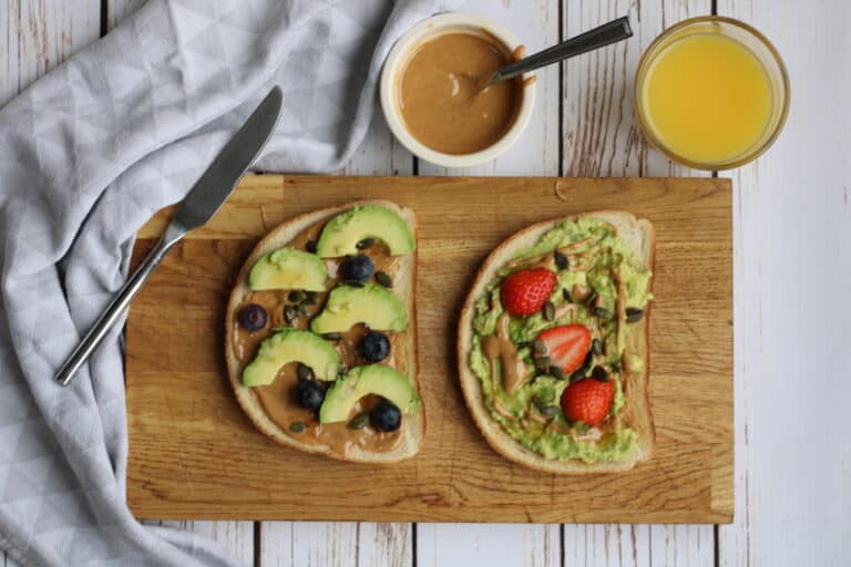 Healthy vegan avocado toast with peanut butter and fresh fruit toppings.