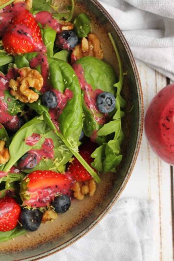 Blueberry strawberry salad with vegan poppy seed dressing, walnuts, and spinach in a rustic bowl.