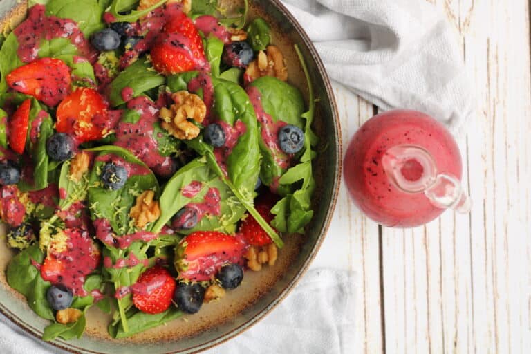 Blueberry strawberry salad with vegan poppy seed dressing, walnuts, and spinach in a rustic bowl.