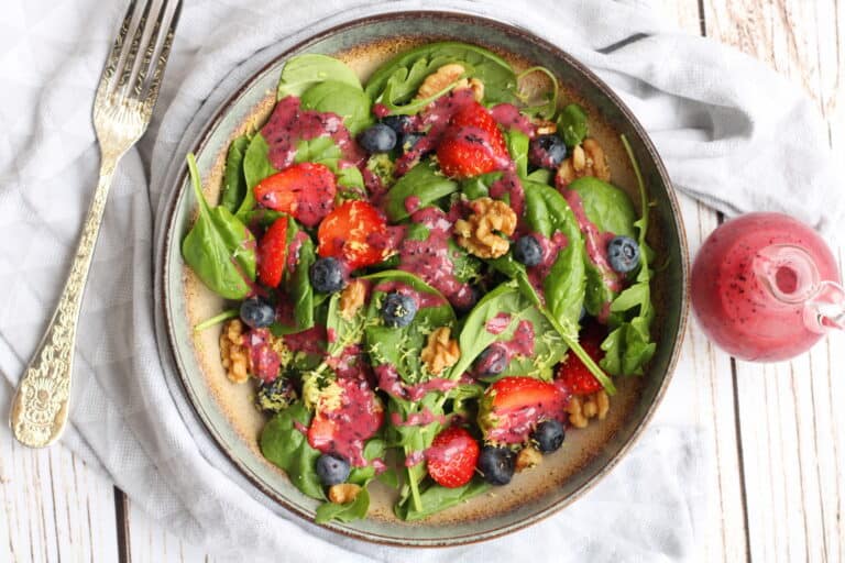 An image of a fresh vegan salad topped with blueberries, strawberries, and walnuts, drizzled with bl.