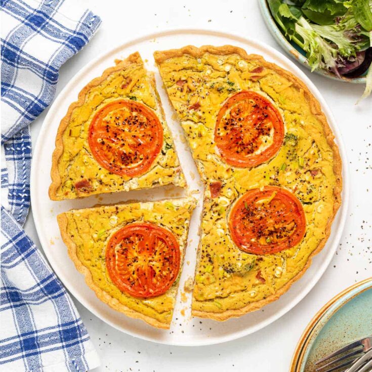 Delicious vegan tomato quiche with fresh tomatoes and herbs on a white plate.