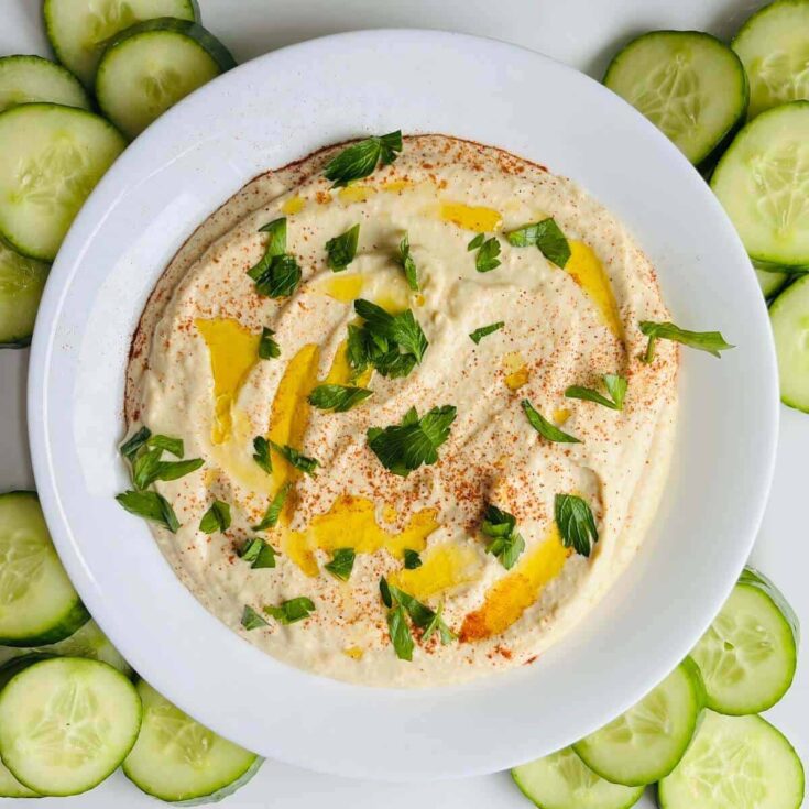 Vegan hummus served with fresh cucumber slices and herbs.