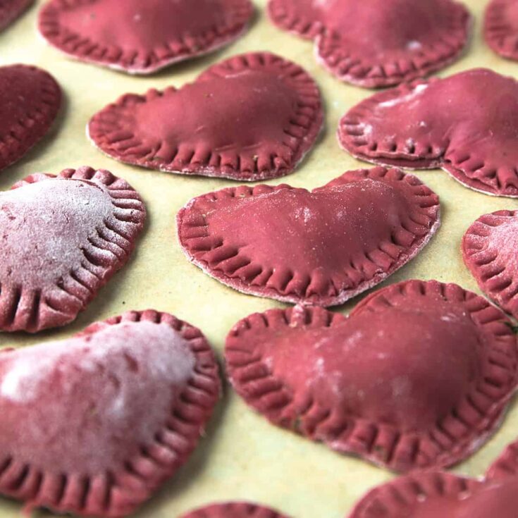 Vegan heart-shaped cookies with pink and purple icing on parchment paper.