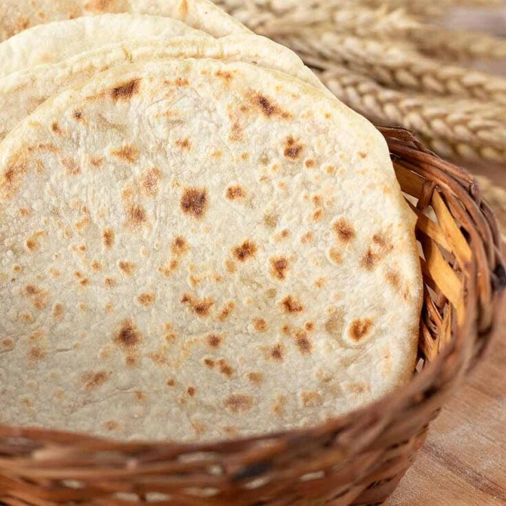 Fresh whole wheat flatbread in a woven basket on a wooden surface.
