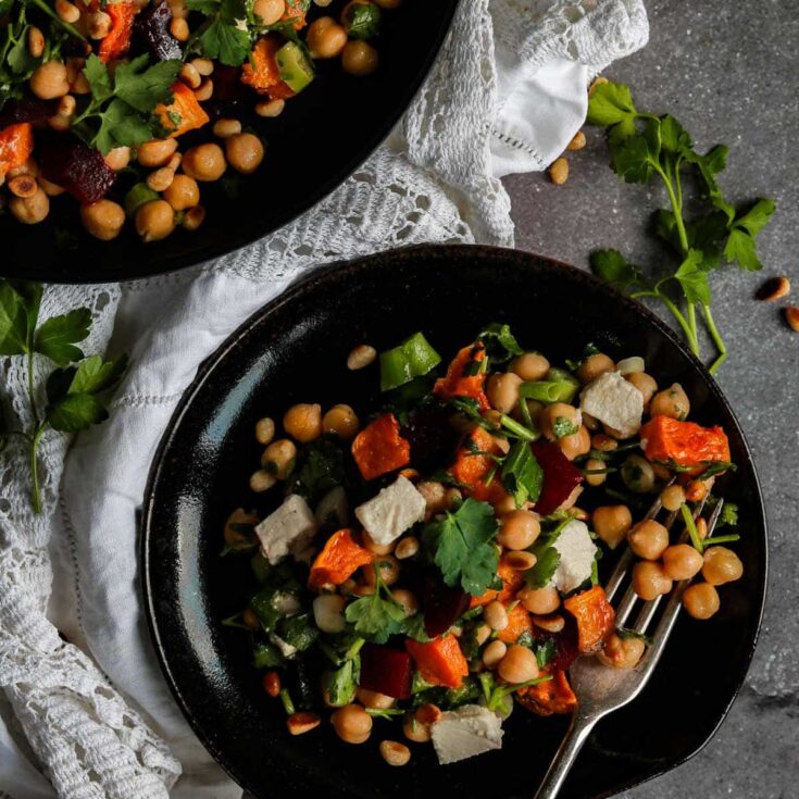Vegan chickpea and vegetable salad with fresh herbs on black plate.