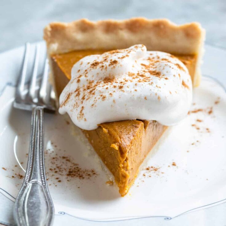 Delicious vegan pumpkin pie topped with whipped coconut cream and cinnamon.