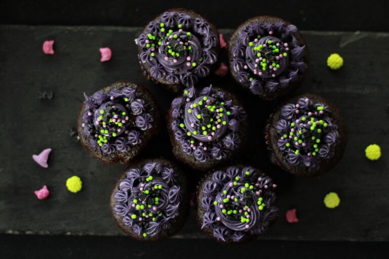 Vegan Halloween cupcakes decorated with purple frosting and green sprinkles for a spooky celebration.