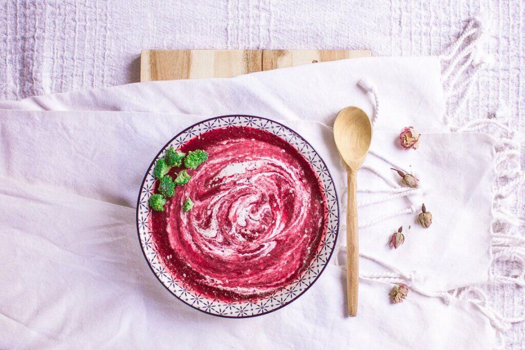 Vibrant vegan beetroot soup in a decorative bowl with fresh herbs.