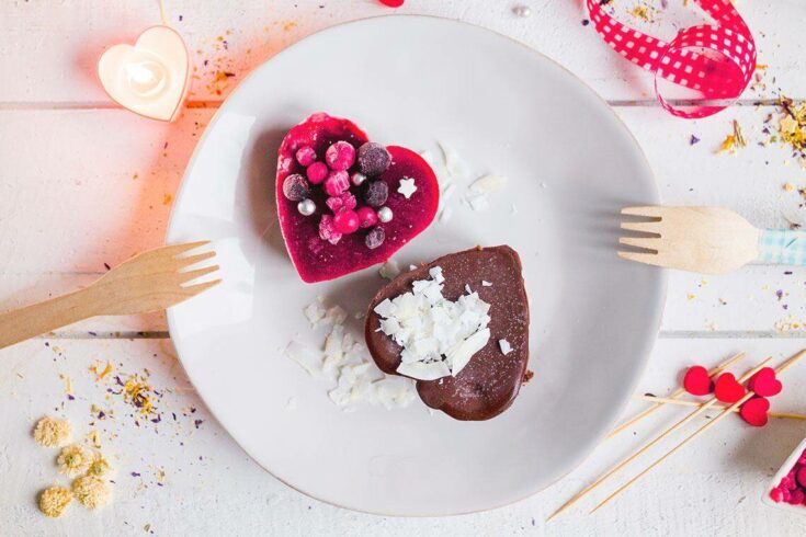 Vegan heart-shaped desserts with berries and chocolate on a white plate.