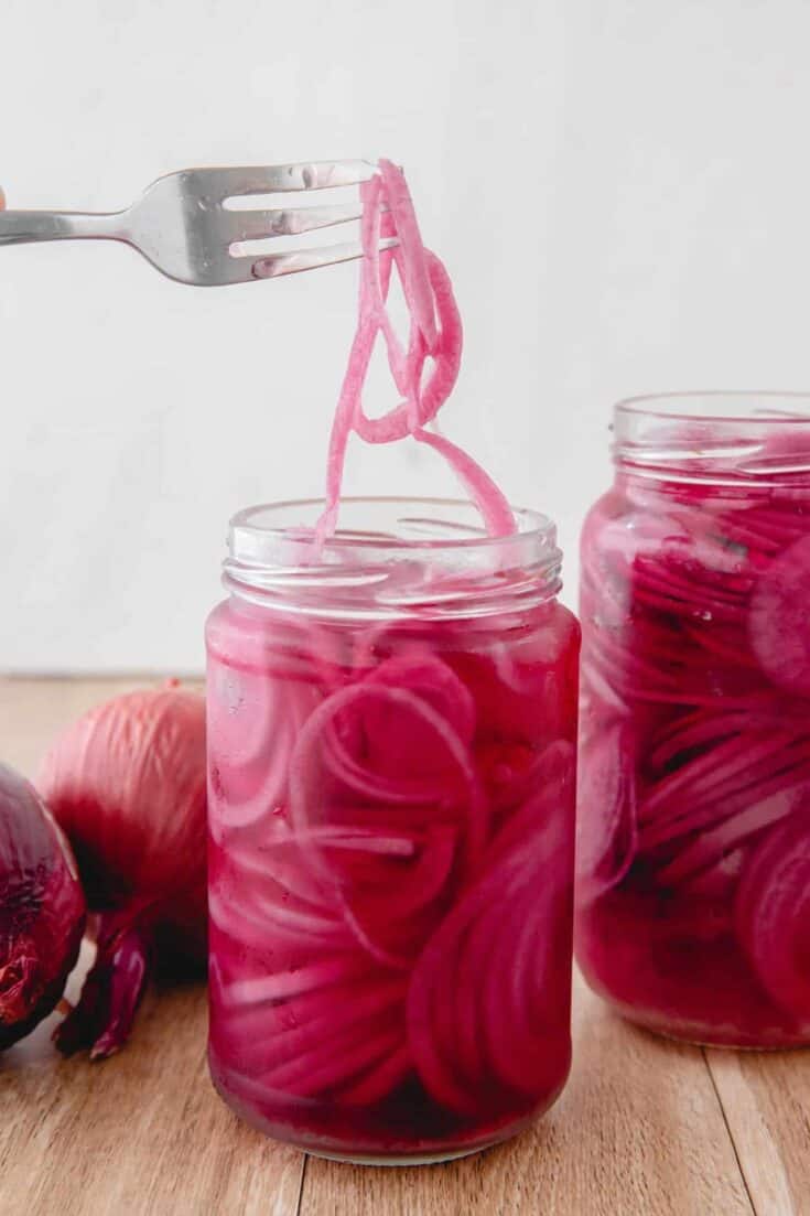 Bright pink pickled onions in glass jars, perfect for vegan salads and sandwiches.